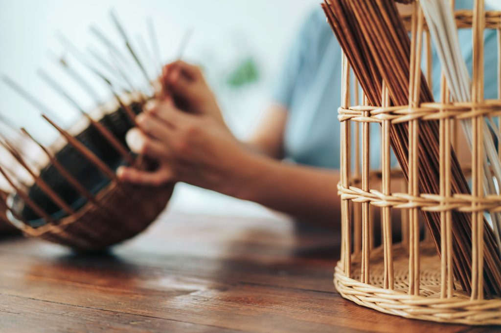 Woman weaves basket of paper tubes on wooden table